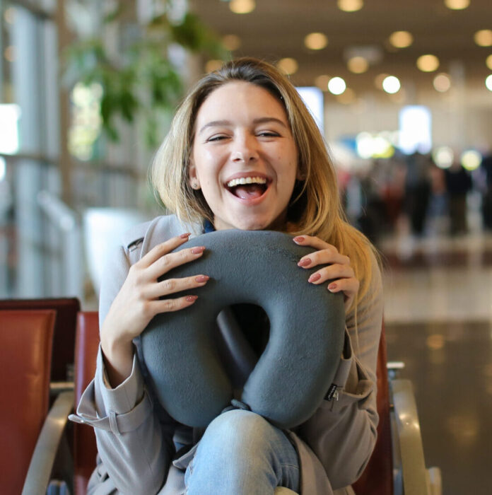 Woman sitting with neck pillow and luggage in airport waiting room.