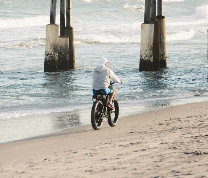 Cyclist riding under a pier on the beach