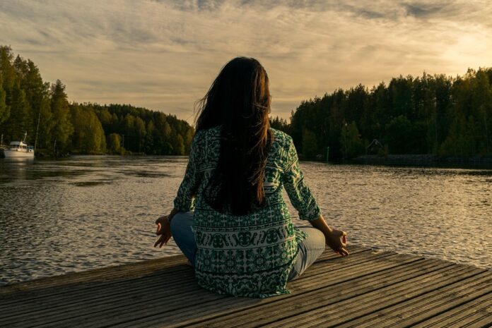 Woman meditating on a pier at a lake