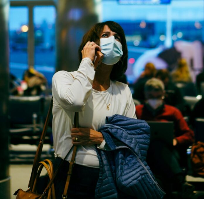 Worried woman wearing a mask speaking on phone at the airport